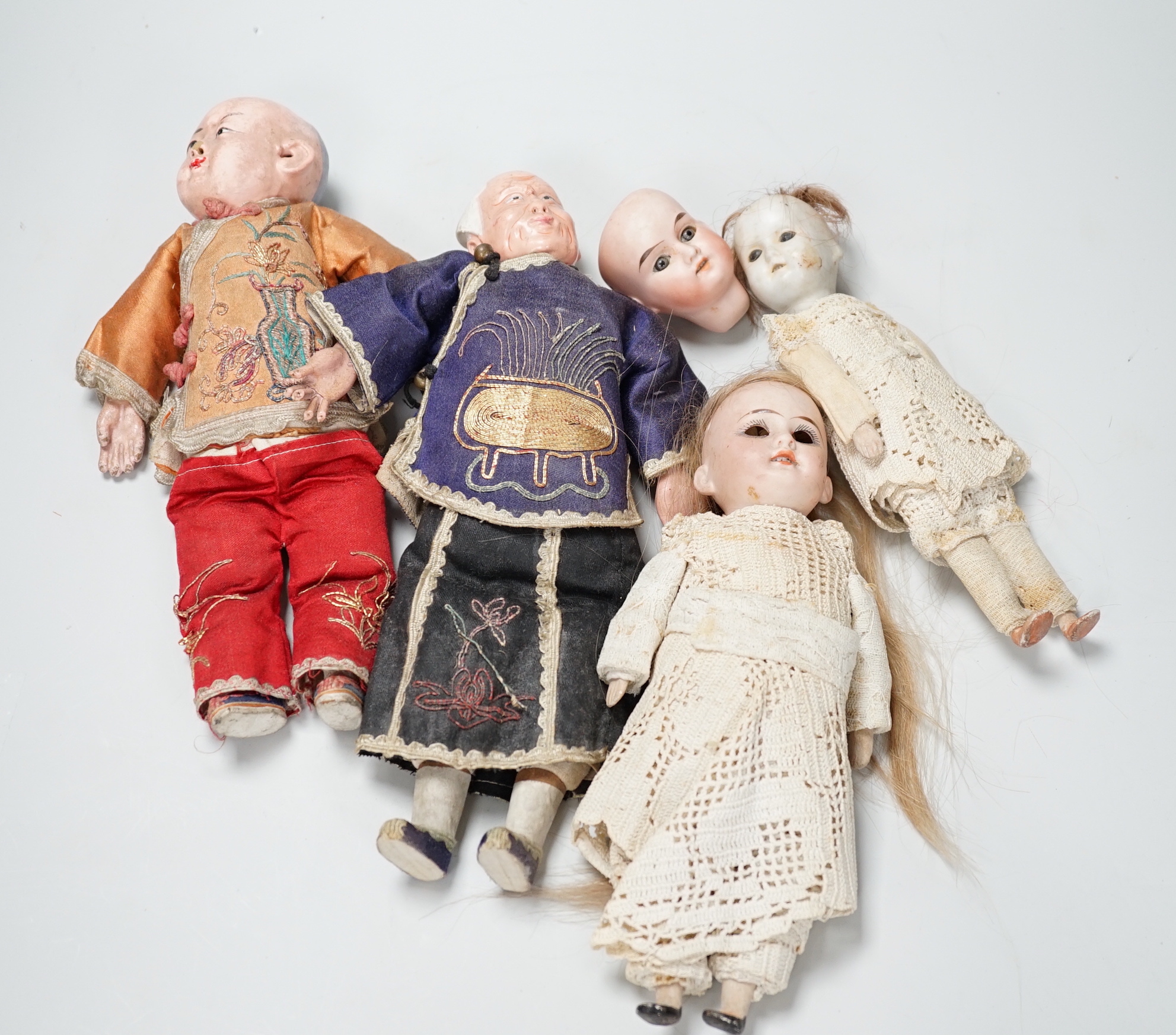 Two Chinese Papier mache dolls with embroidered silk clothing, a pair of Chinese embroidered silk slippers, a similar child’s bonnet a pair of Japanese slippers and three other dolls